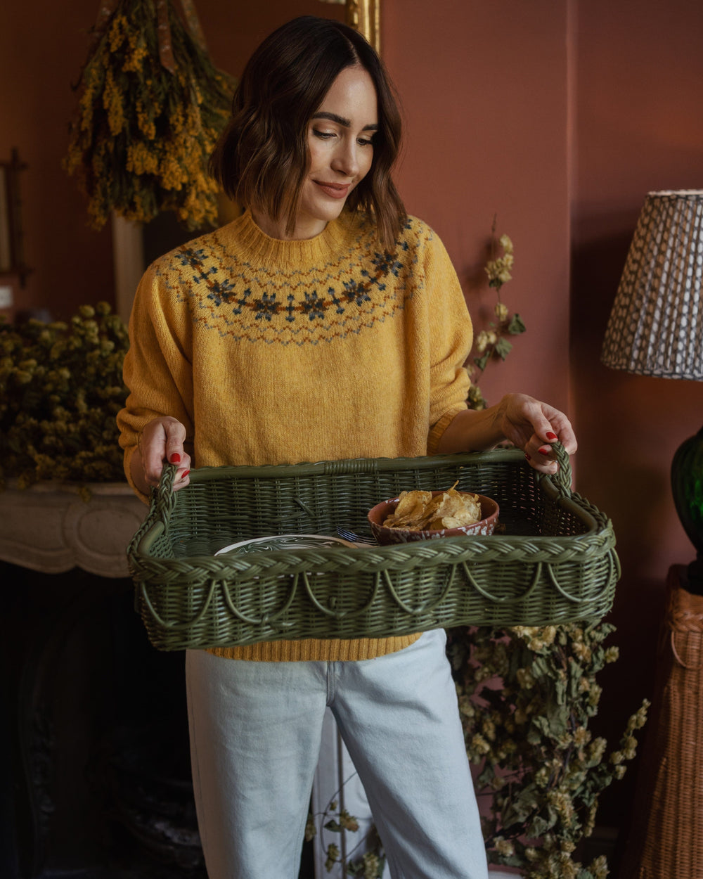 Front view of Hadley Tray in green showcasing braided scalloped edge and fixed handles while held by a model in a warm indoor setting