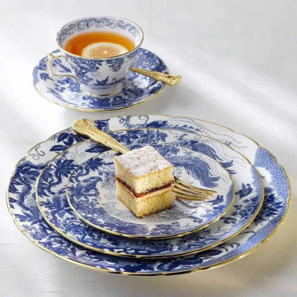 Front view of Aves blue fine bone china stack of plates and teacup showcasing bird and floral pattern with scalloped 22 carat gold rims on white background