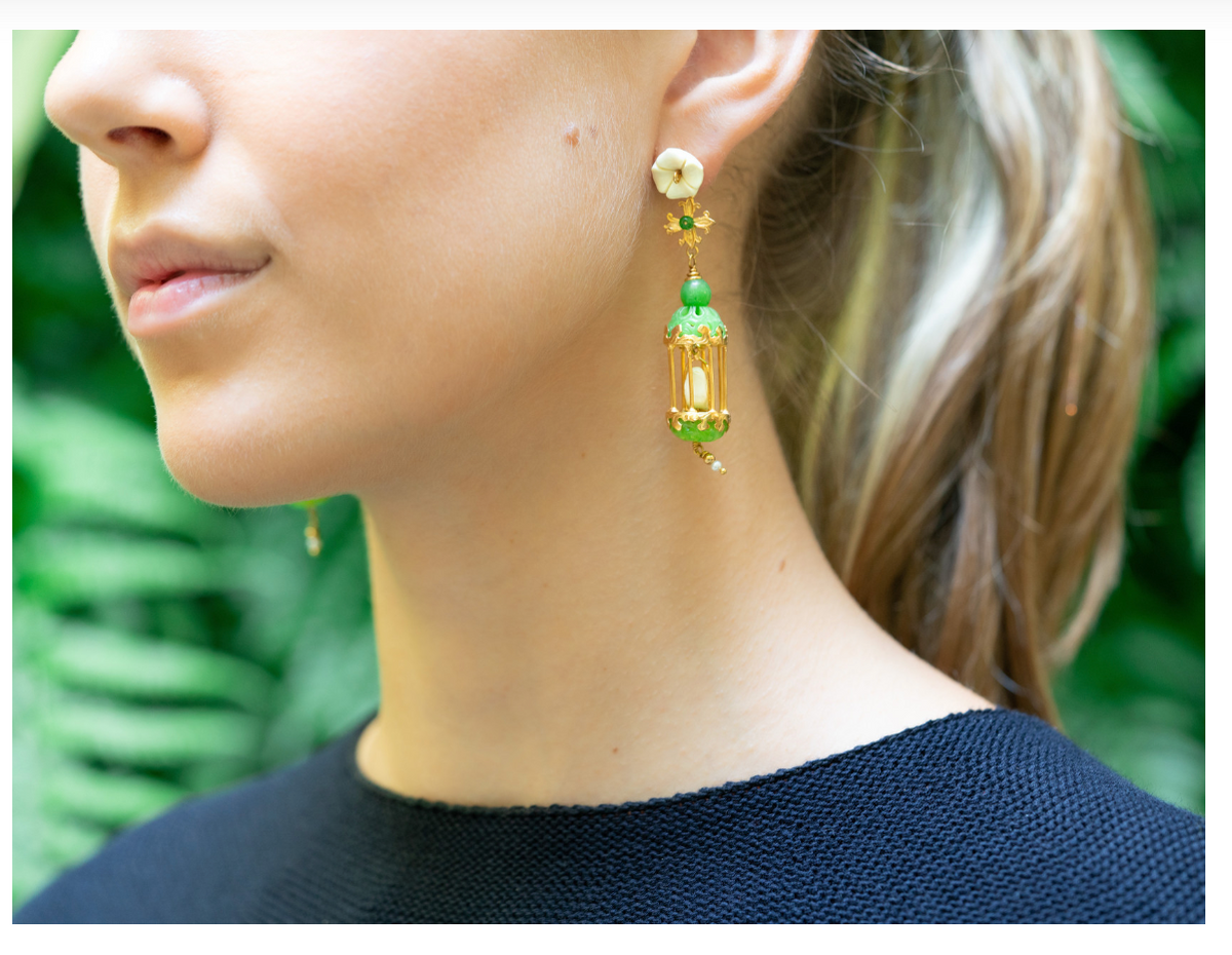 Side close up of Aviary Classic Mini earring showing white flower stud and jade and gold pendant against blurred greenery