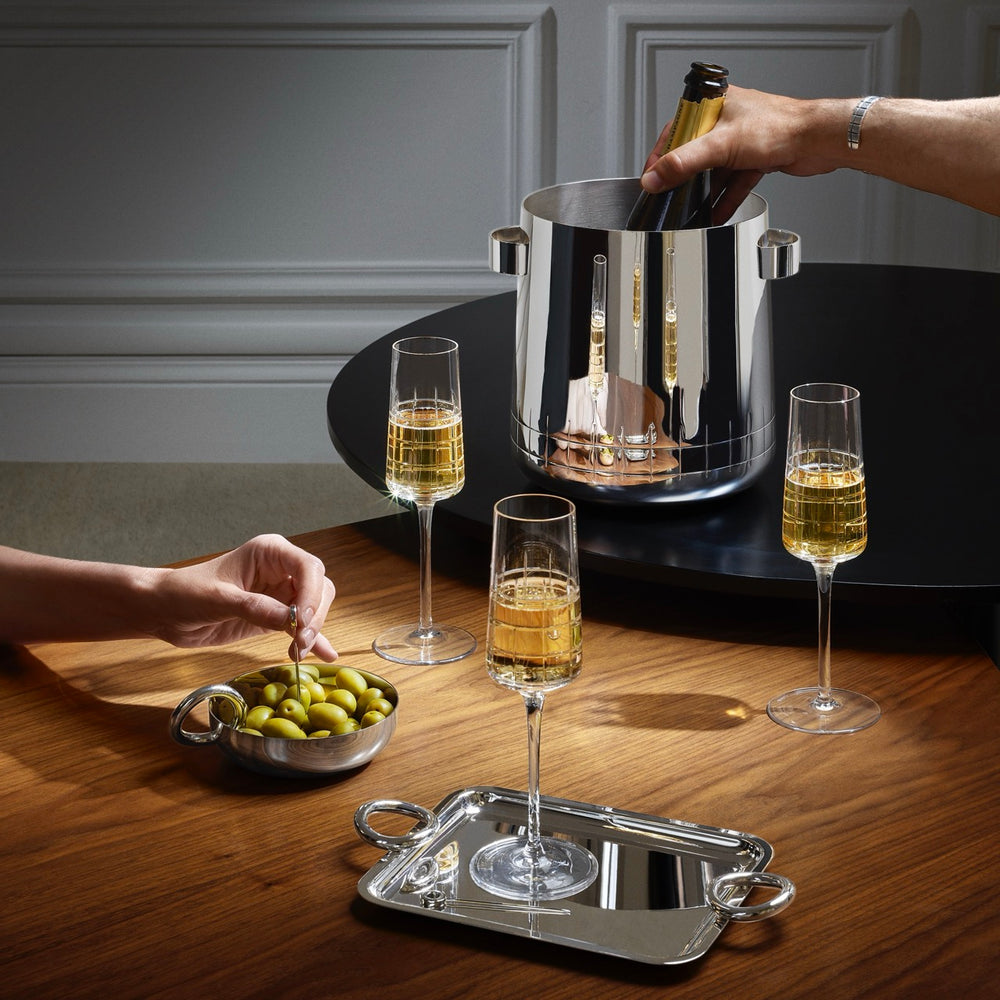Small Vertigo silver-plated tray with ring handles holding a champagne glass on a wooden table with olives and an ice bucket in the background