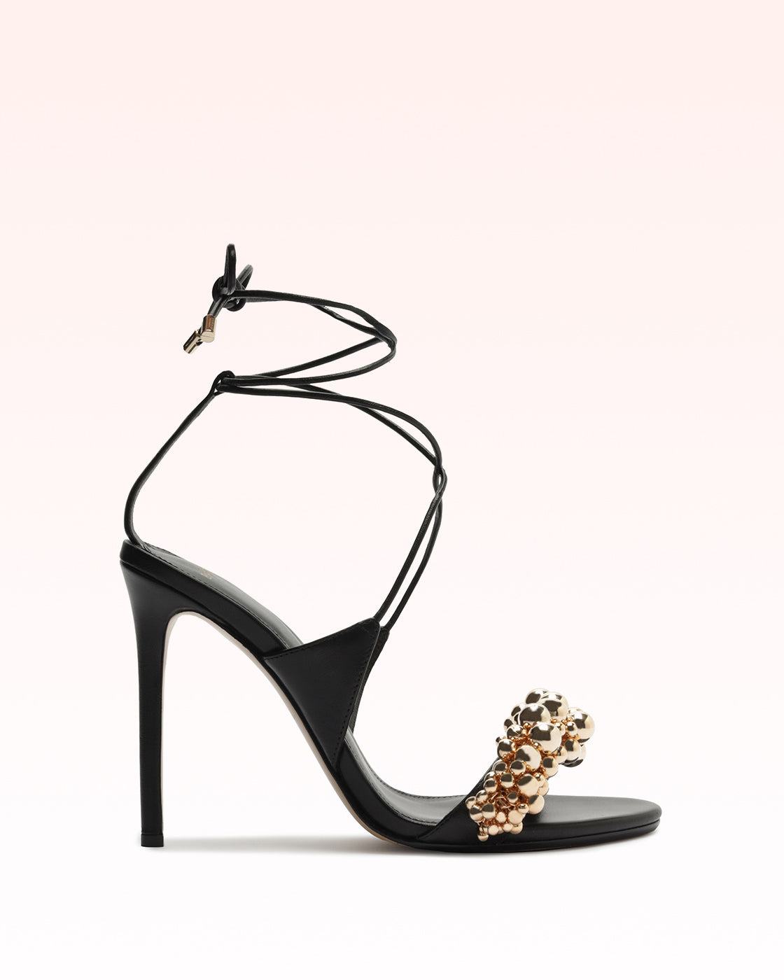 Side view of Gia 100 in Black showcasing gold beaded toe detail and ankle wrap laces on a light background