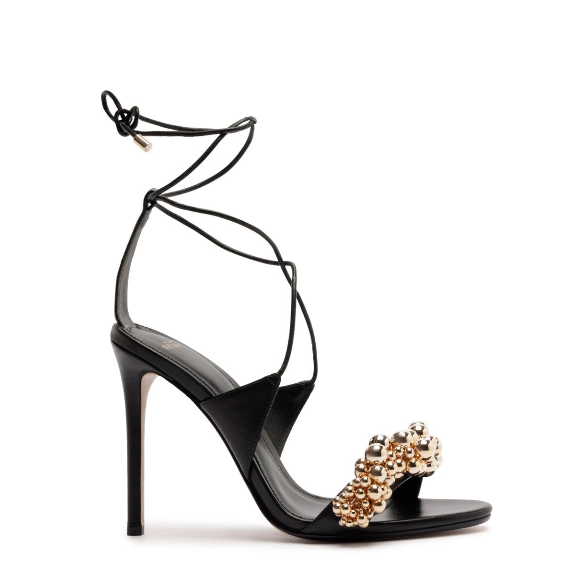 Side view of Gia 100 black leather stiletto with ankle wrap laces and gold beaded toe strap on white background