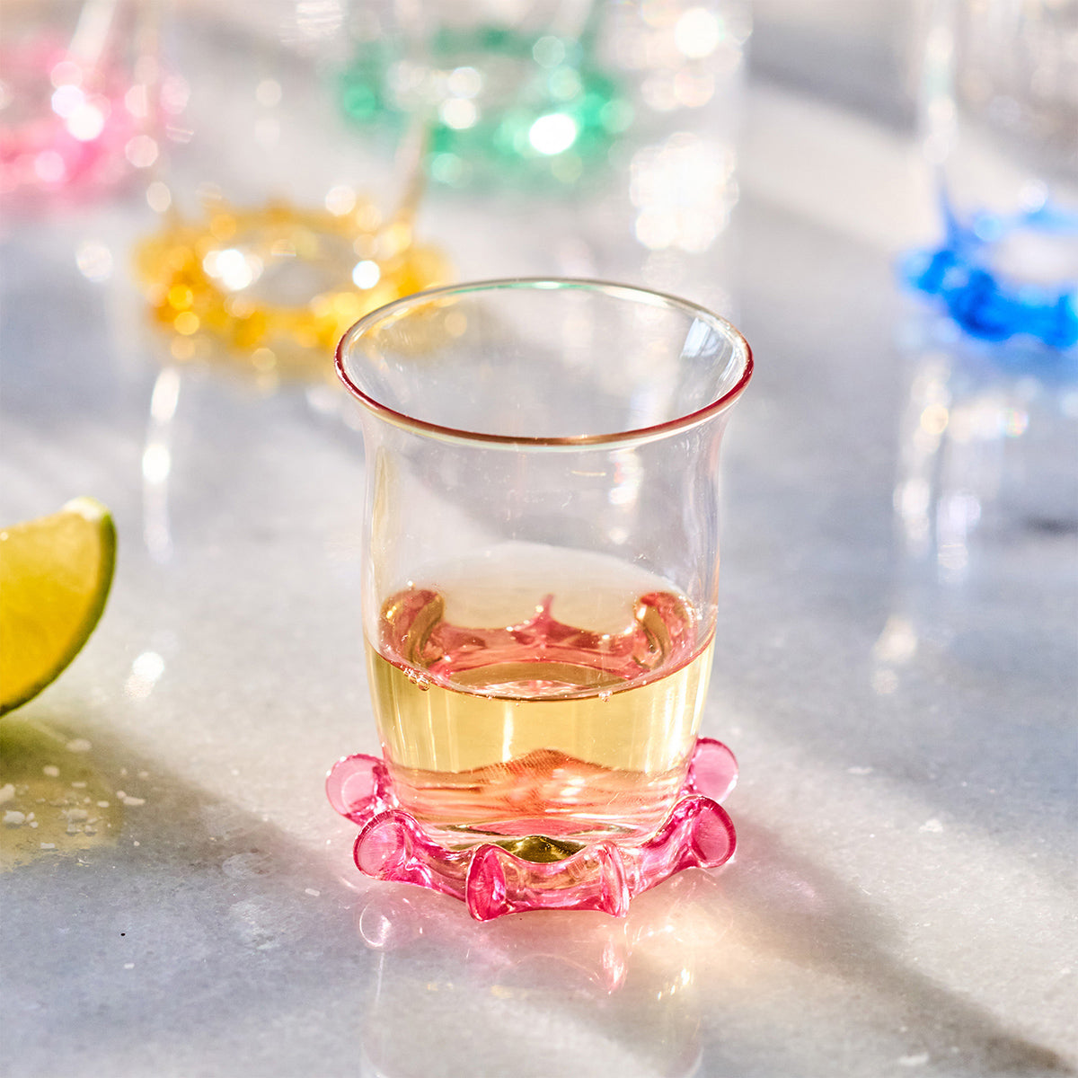 Front view of Harriet Shot Glass in Blush showcasing its sculptural pink ruffle trim with a drink on a reflective table