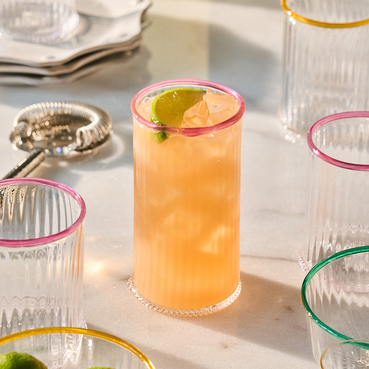 Front view of Nell Highball in Blush showcasing its pink rim and textured glass with a cocktail on a table