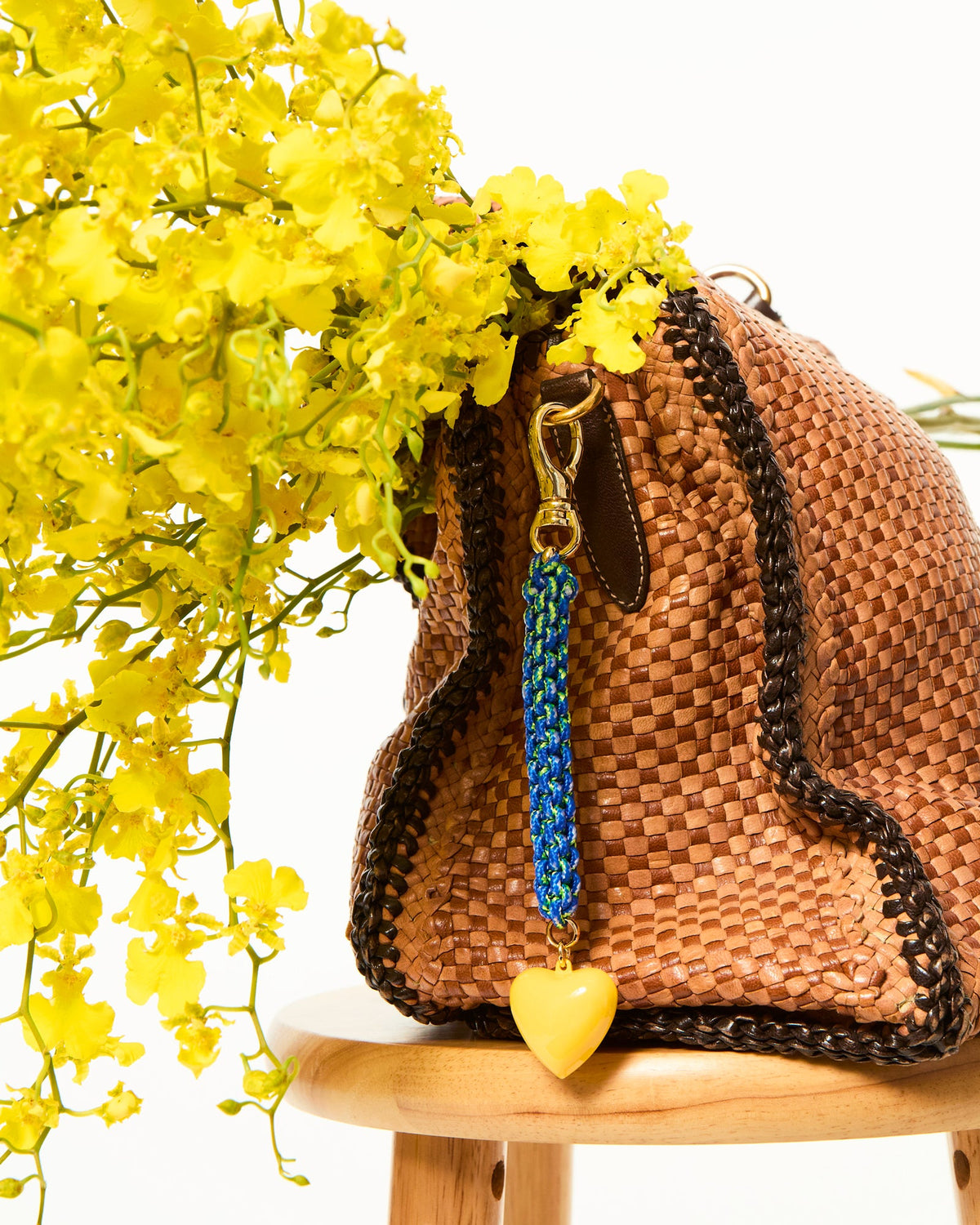 Close-up of The Happy Cord Bag Charm showcasing blue beaded cord and yellow enamel heart on a woven handbag