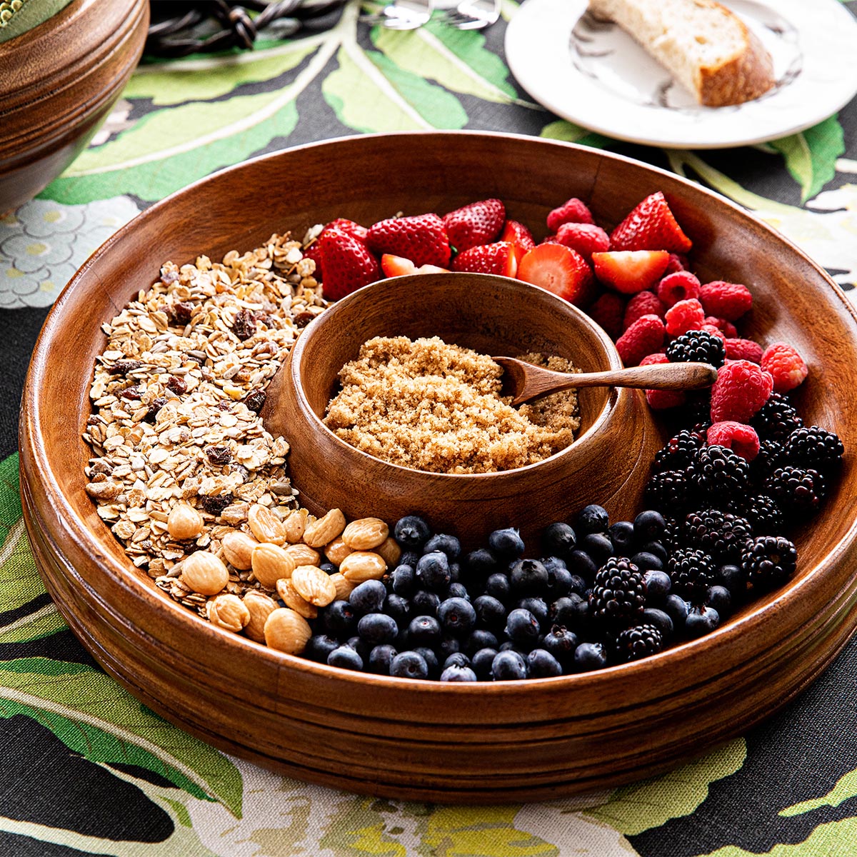Close-up of Bilbao wood chip and dip showing central bowl and divided tray with berries, nuts, and granola on a patterned tablecloth