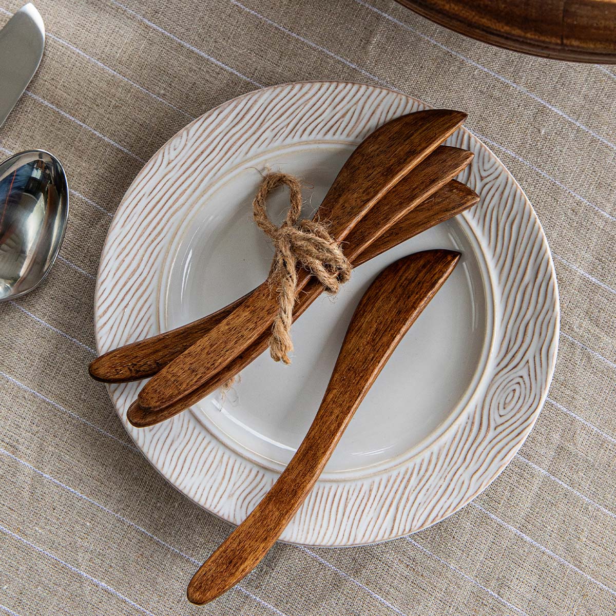 Top-down view of Bilbao wood spreaders showing warm mango wood grain tied with twine on a white textured plate