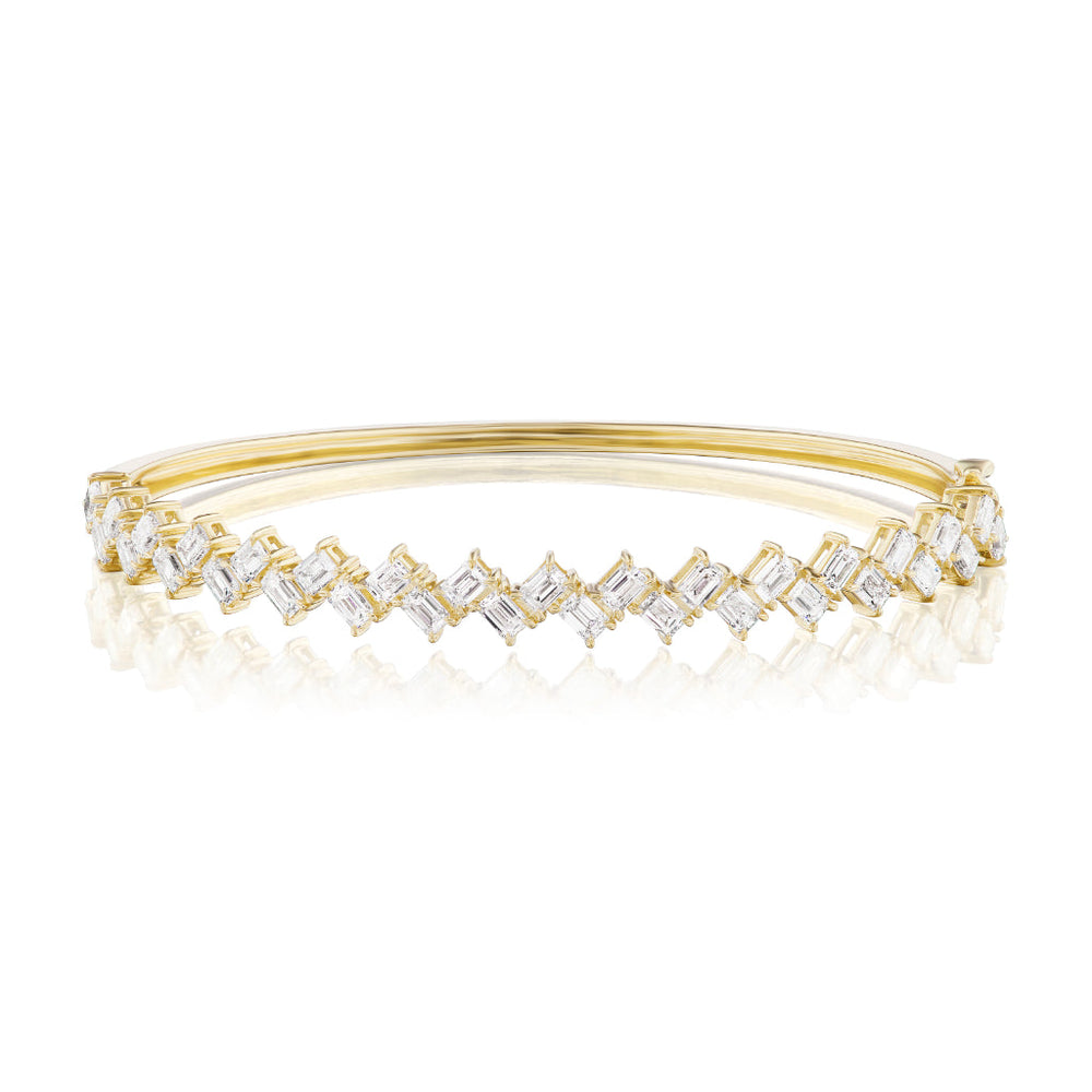 The Zig Zag Motif Emerald Cut Diamond Bangle showcases a row of emerald cut diamonds in a zigzag design, crafted from polished 18k gold with a sleek, reflective finish.