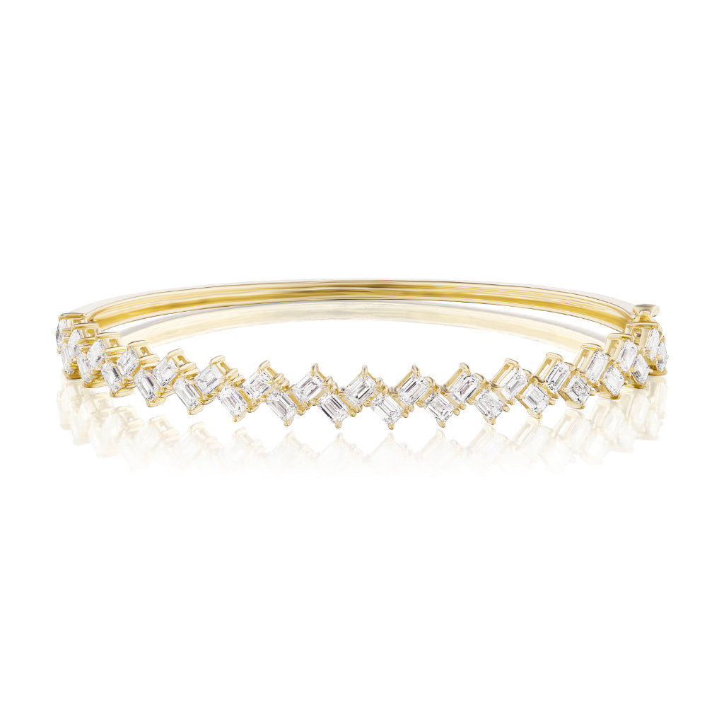 The Zig Zag Motif Emerald Cut Diamond Bangle showcases a row of emerald cut diamonds in a zigzag design, crafted from polished 18k gold with a sleek, reflective finish.
