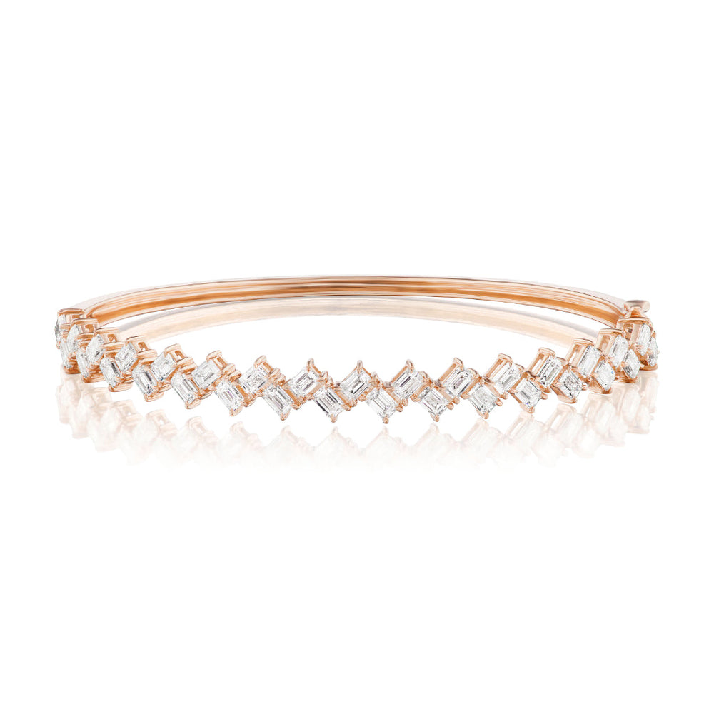 The Zig Zag Motif Emerald Cut Diamond Bangle is a rose gold bracelet featuring two rows of angular, emerald-cut white diamonds with VS clarity in a zig-zag pattern atop a smooth polished band.