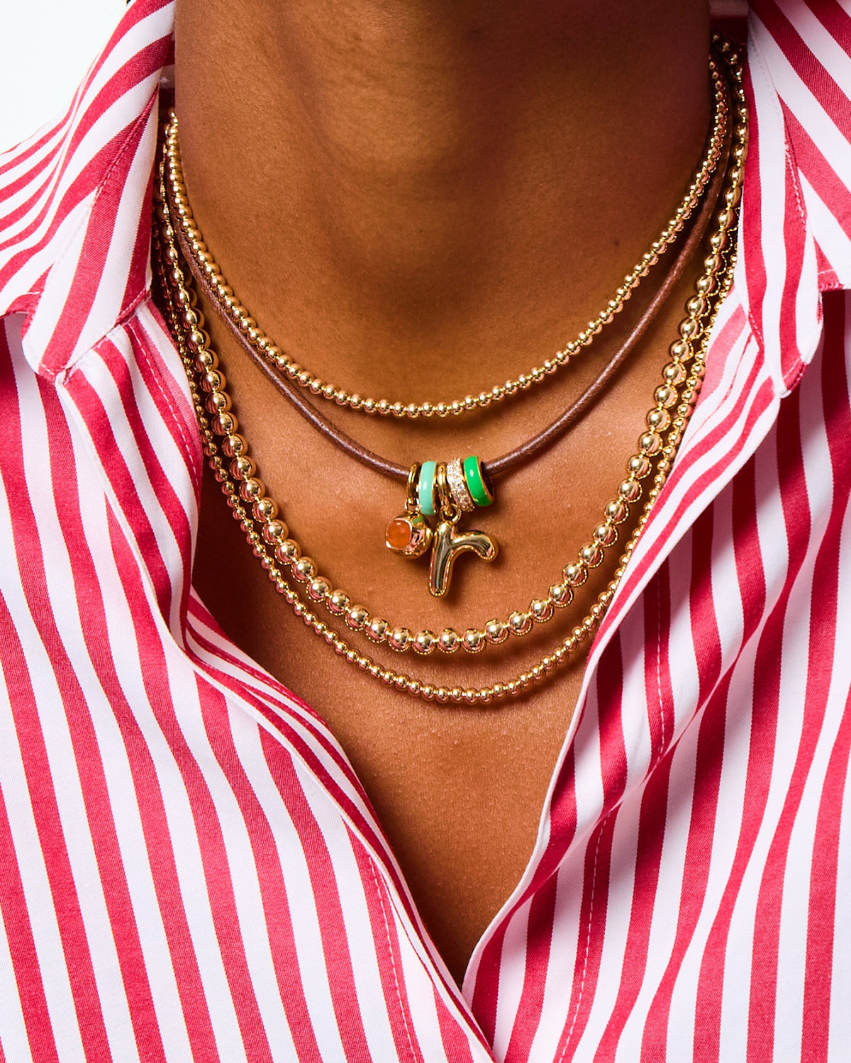 Close-up of The Bigger Bead Necklace in Gold showcasing gold-tone beads and colorful enamel charms on a striped shirt