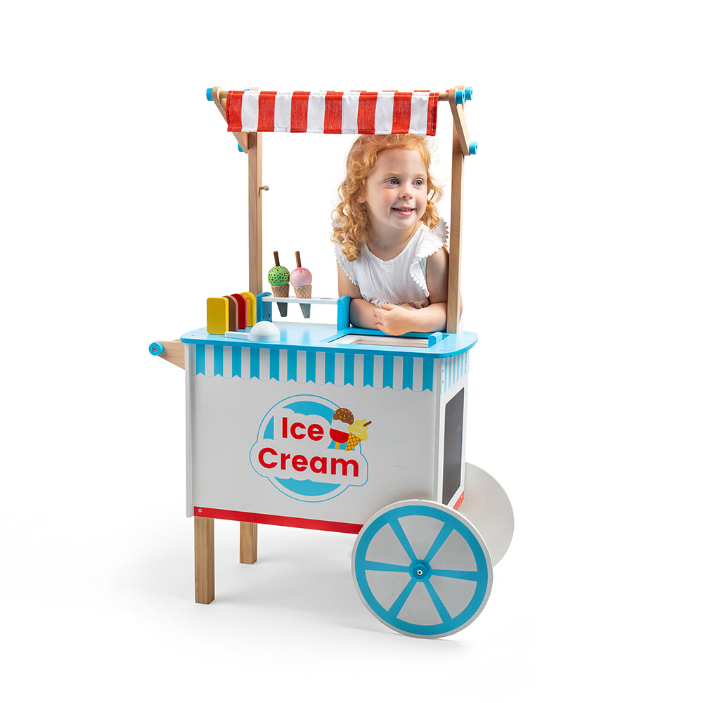 Front view of wooden Ice Cream Cart showcasing striped canopy, serving counter, and toy treats with a child behind it on a white background