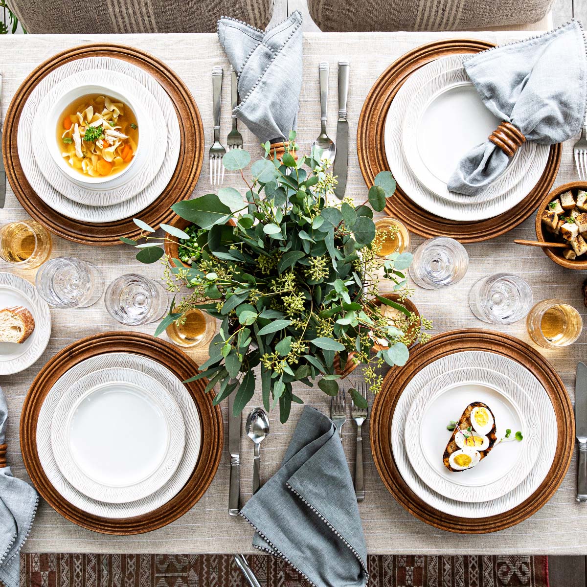 Blenheim Oak tableware arranged on a dining table with food, gray napkins, cutlery, and greenery