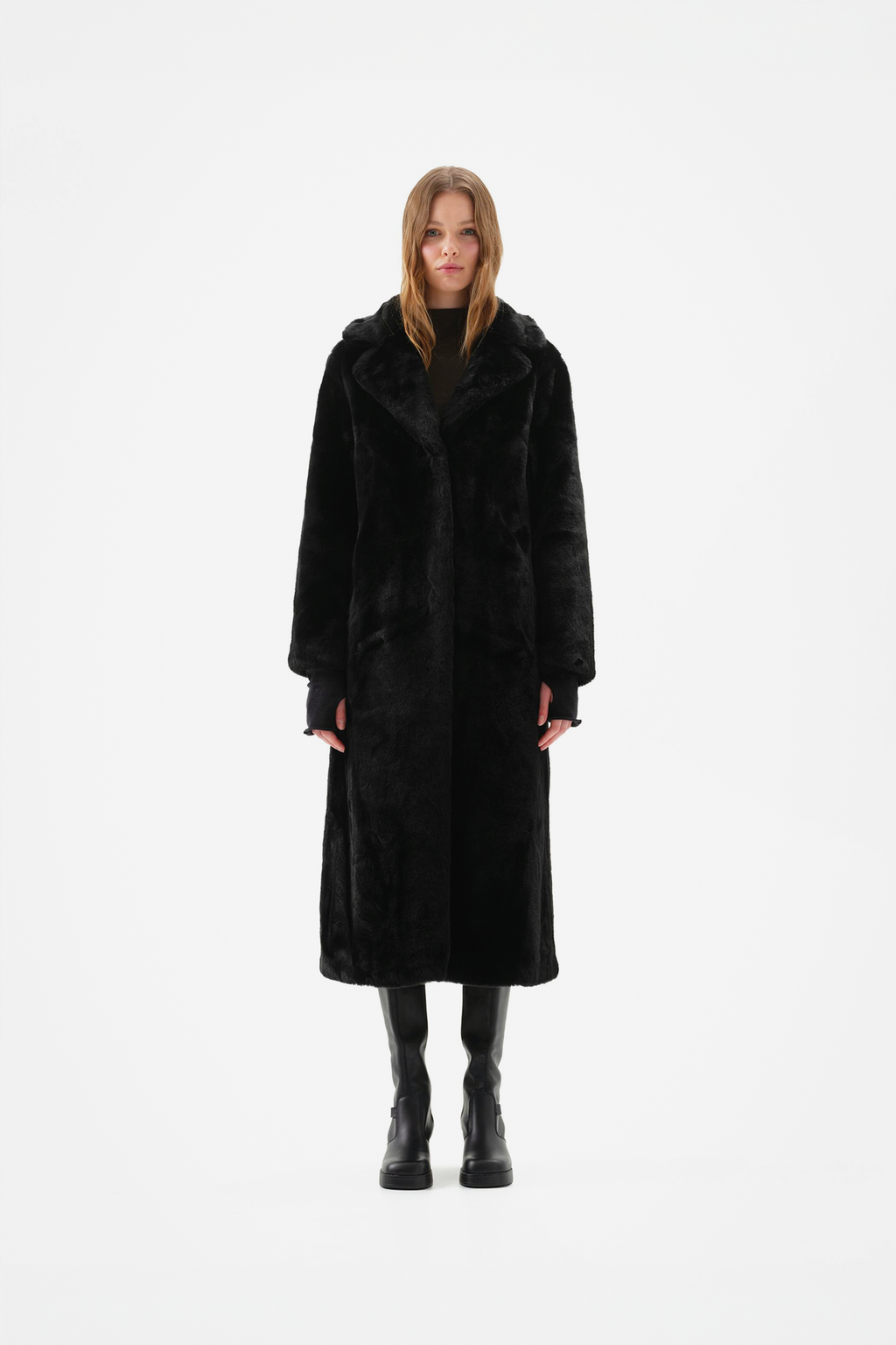 Long black faux fur coat with notch lapel and full-length, relaxed fit, worn over black knee-high boots, front view