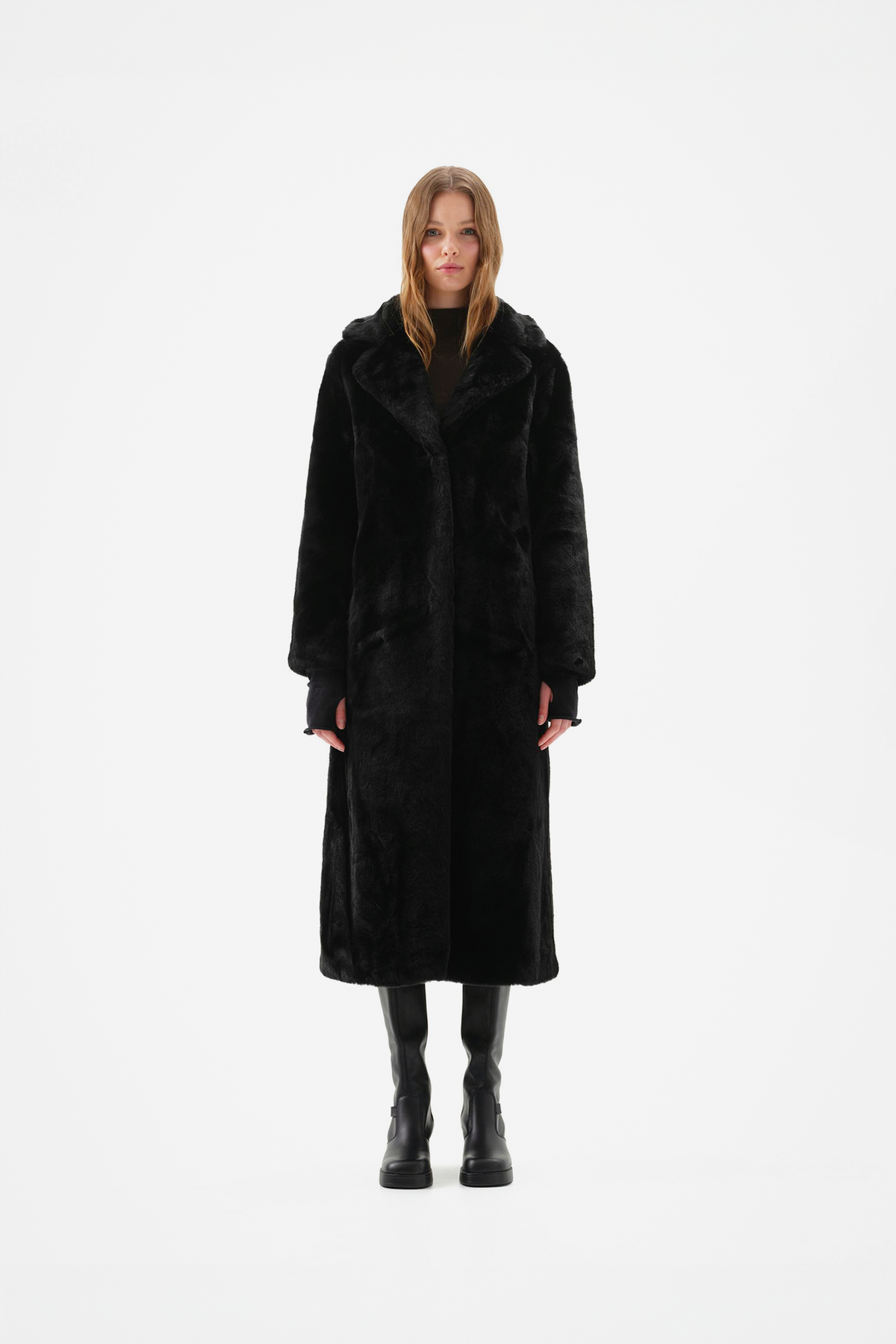 Long black faux fur coat with notch lapel and full-length, relaxed fit, worn over black knee-high boots, front view