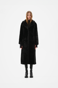 Long black faux fur coat with notch lapel and full-length, relaxed fit, worn over black knee-high boots, front view