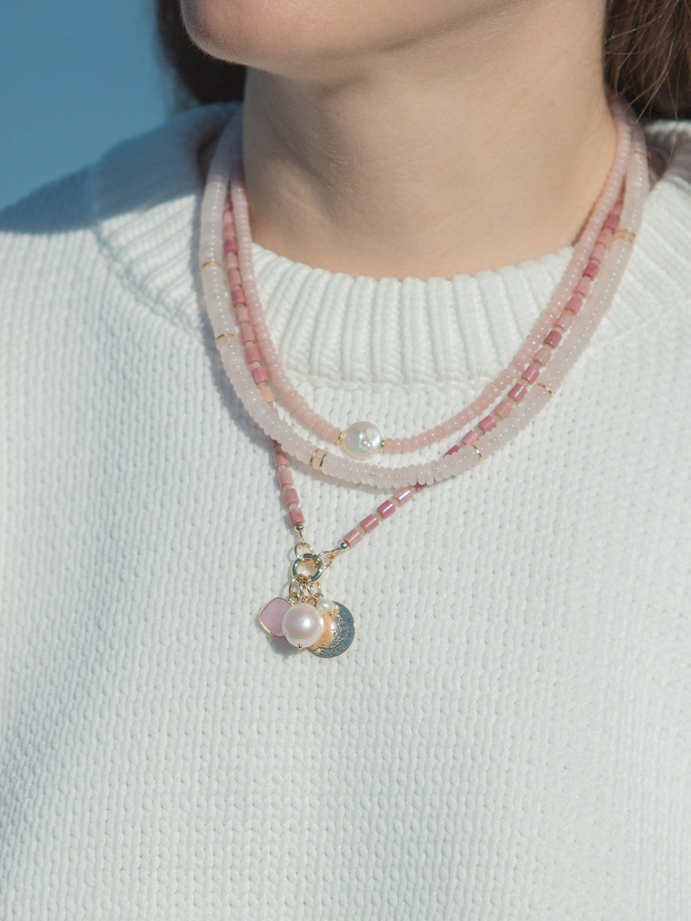 Close-up of Blake Necklace in Pink showing three layered pink opal and bead strands with freshwater pearl and gold charm cluster