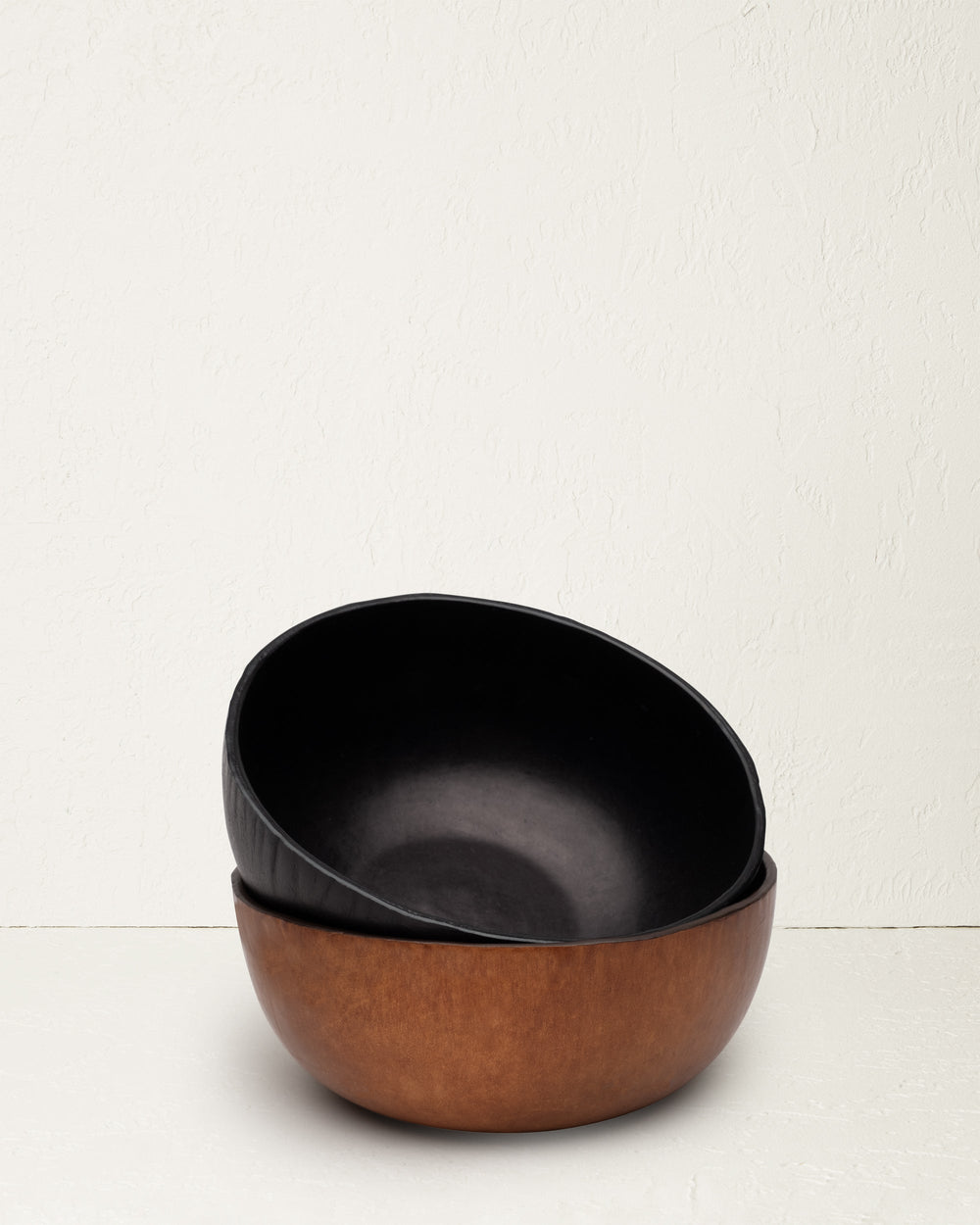 Angled view of The Bowl in black molded leather nested in a brown bowl on a textured off-white surface