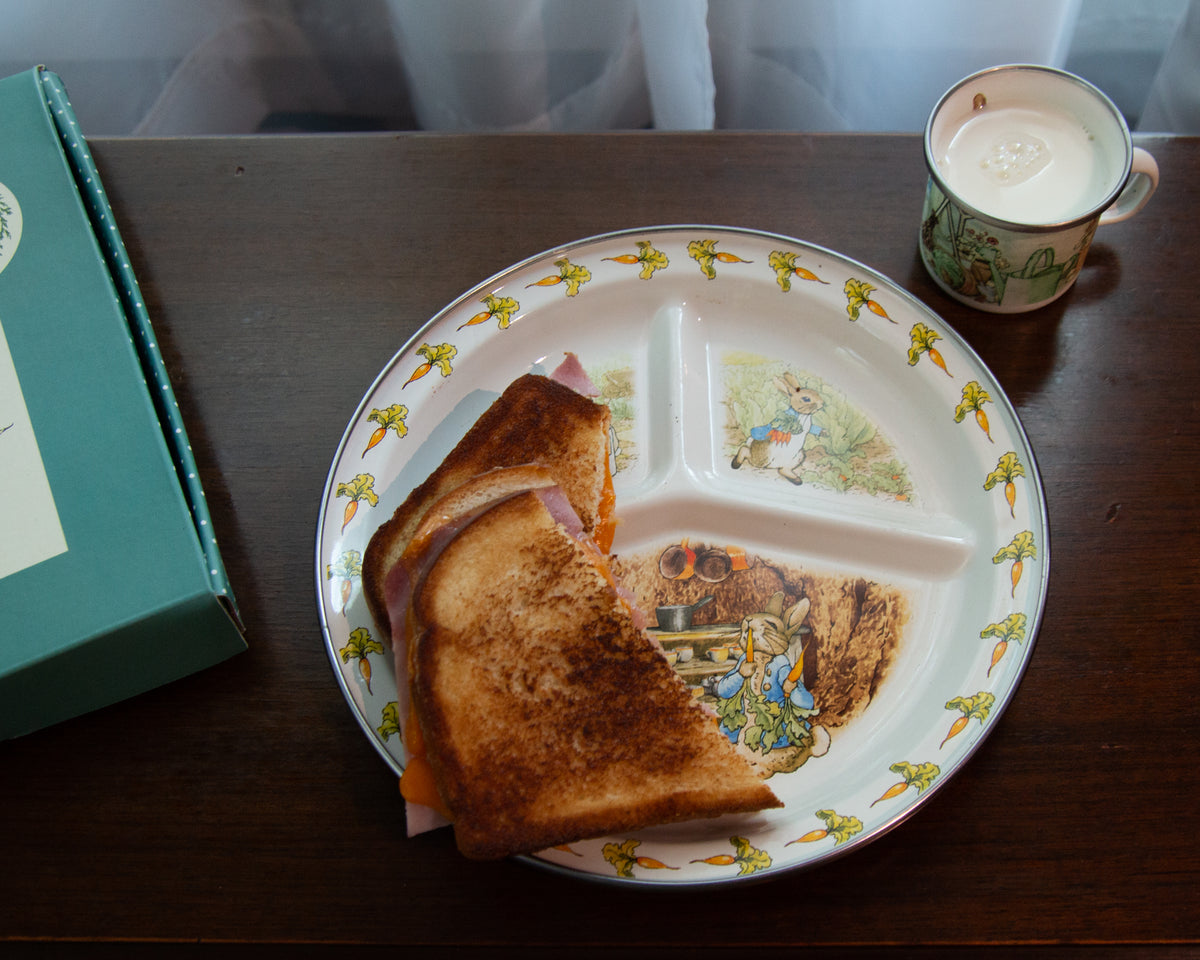 Overhead view of Peter Rabbit Toddler Plate showcasing bunny illustrations and carrot border with sandwich on wooden table
