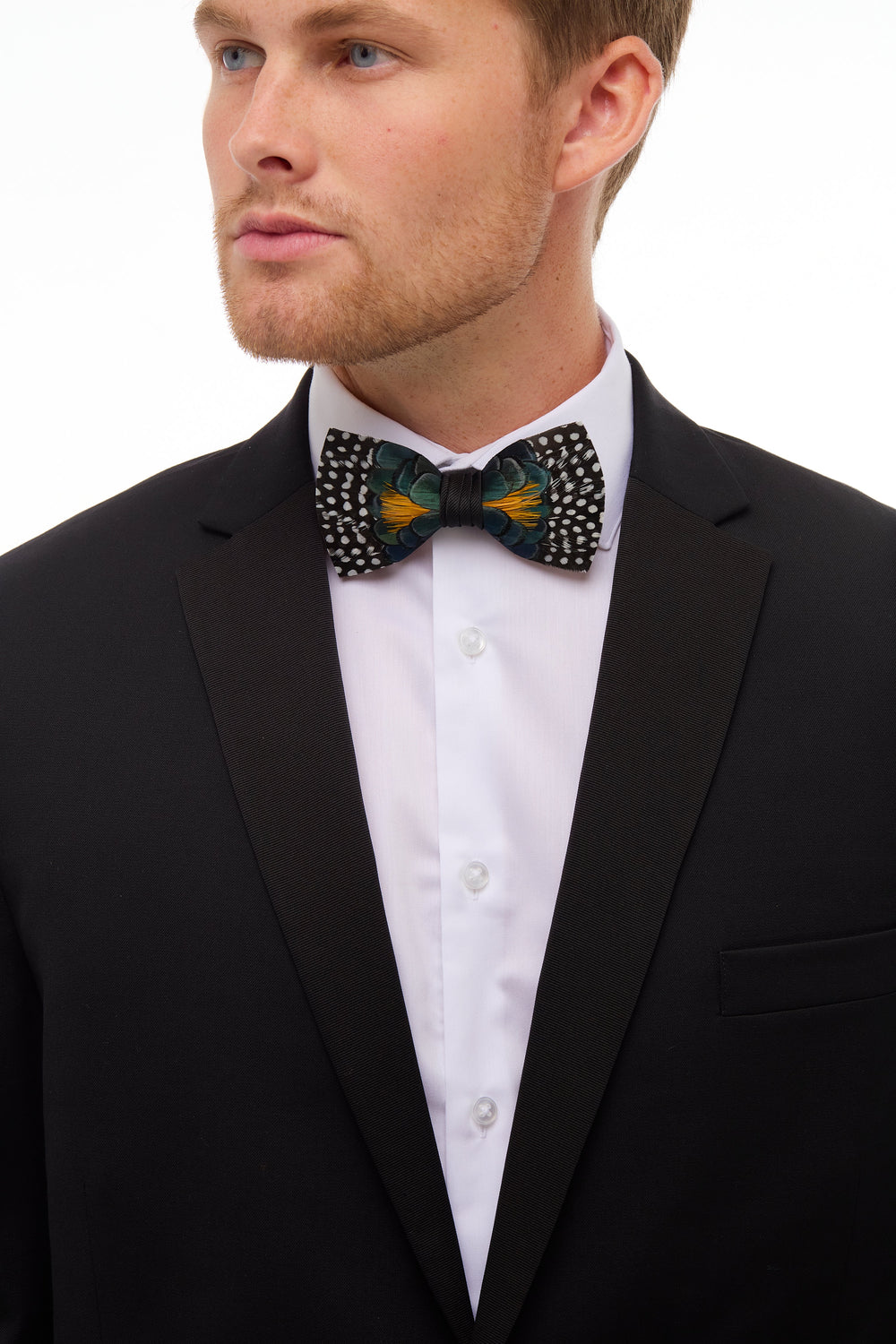 Front view of Owen’s Town bow tie showing spotted feather pattern with teal and orange accents on a model in a black tuxedo