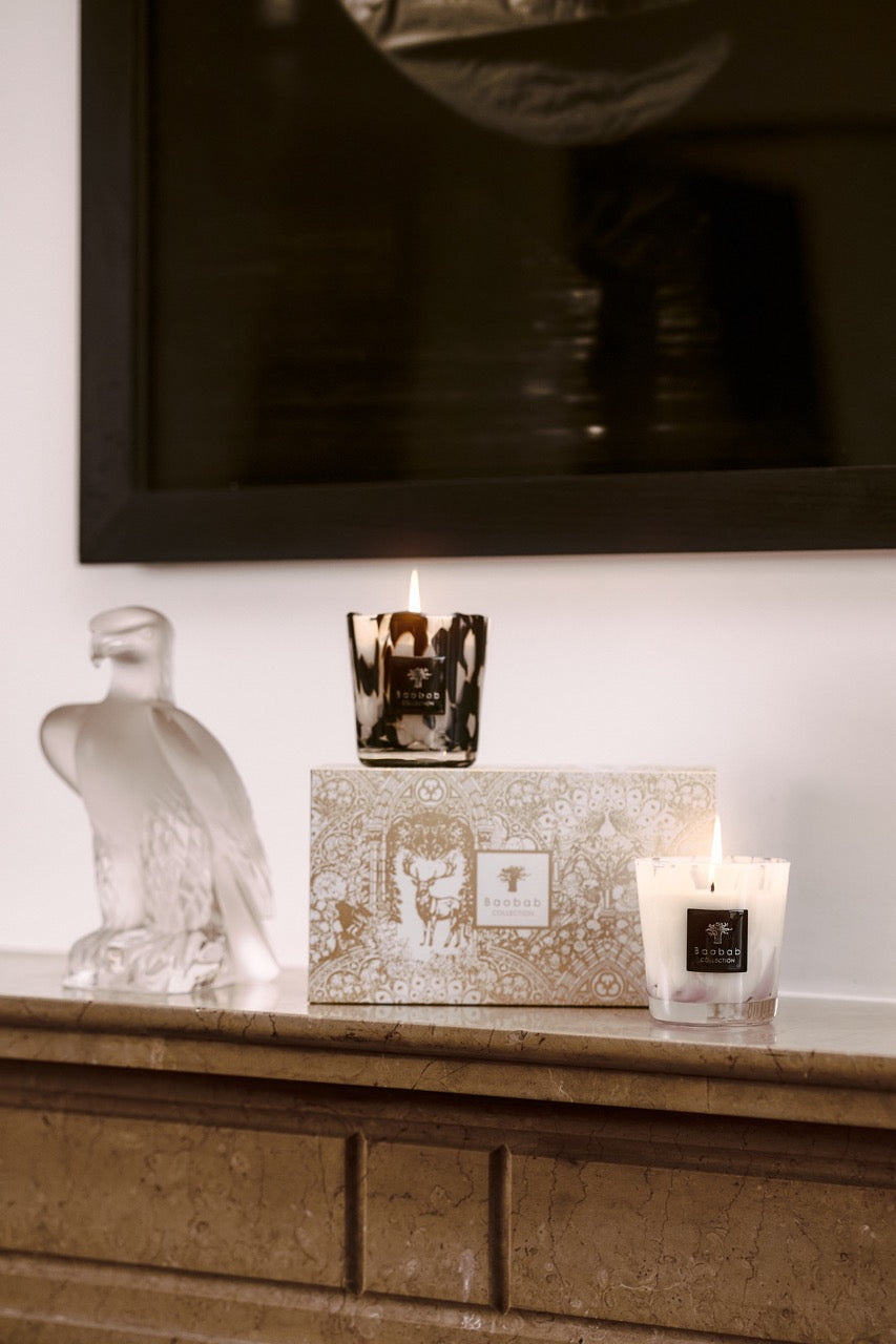Front view of Duo Pearls candle set with lit black marbled candle and lit white candle beside gift box on stone mantel