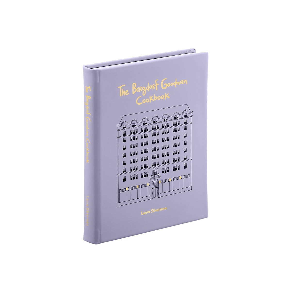 Angled view of The Bergdorf Goodman Cookbook in lilac showcasing its illustrated hardcover with gold lettering on a white background