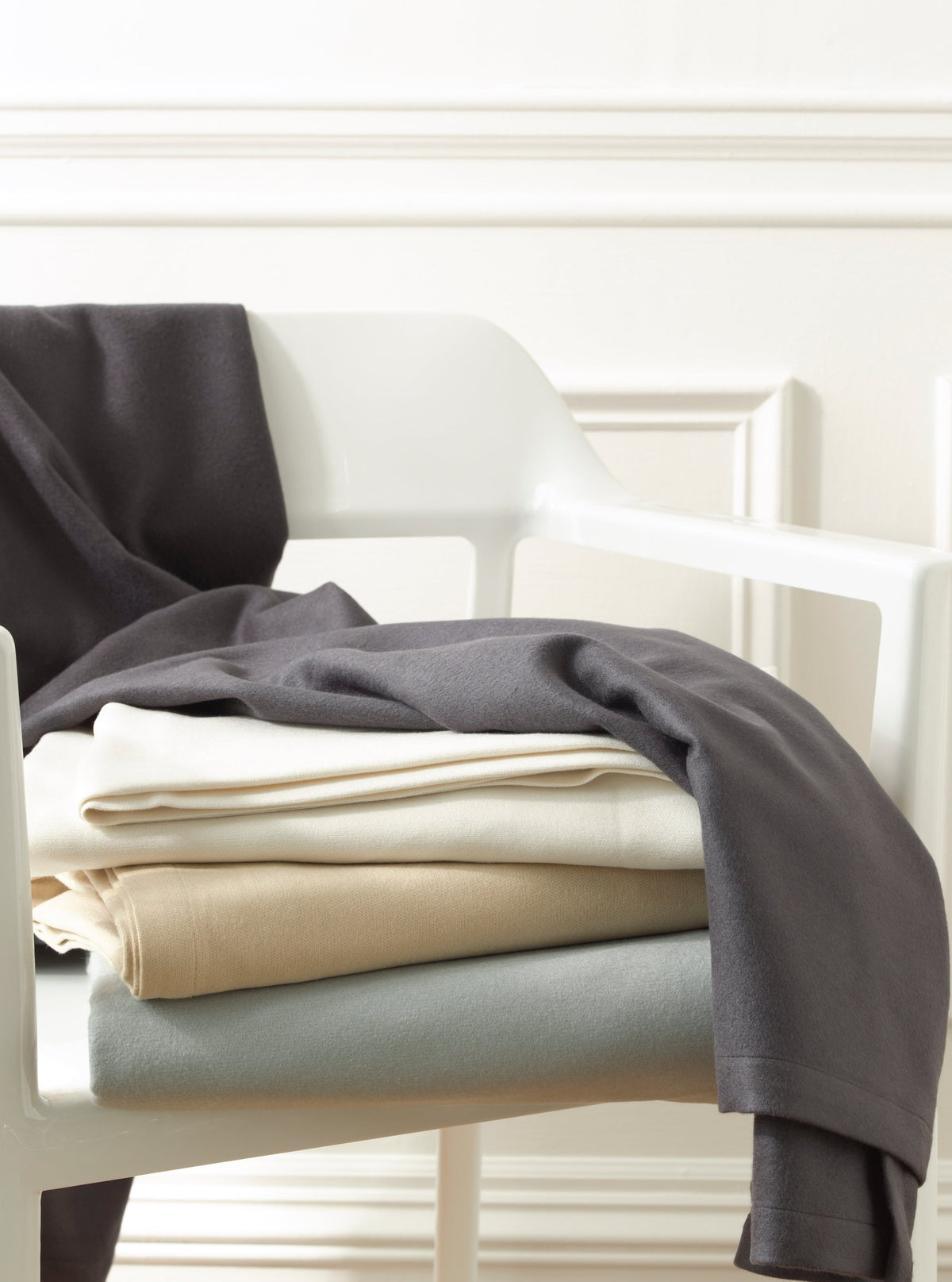 Close up of folded Dream Modal sheets with a charcoal throw on a white chair showing smooth fabric