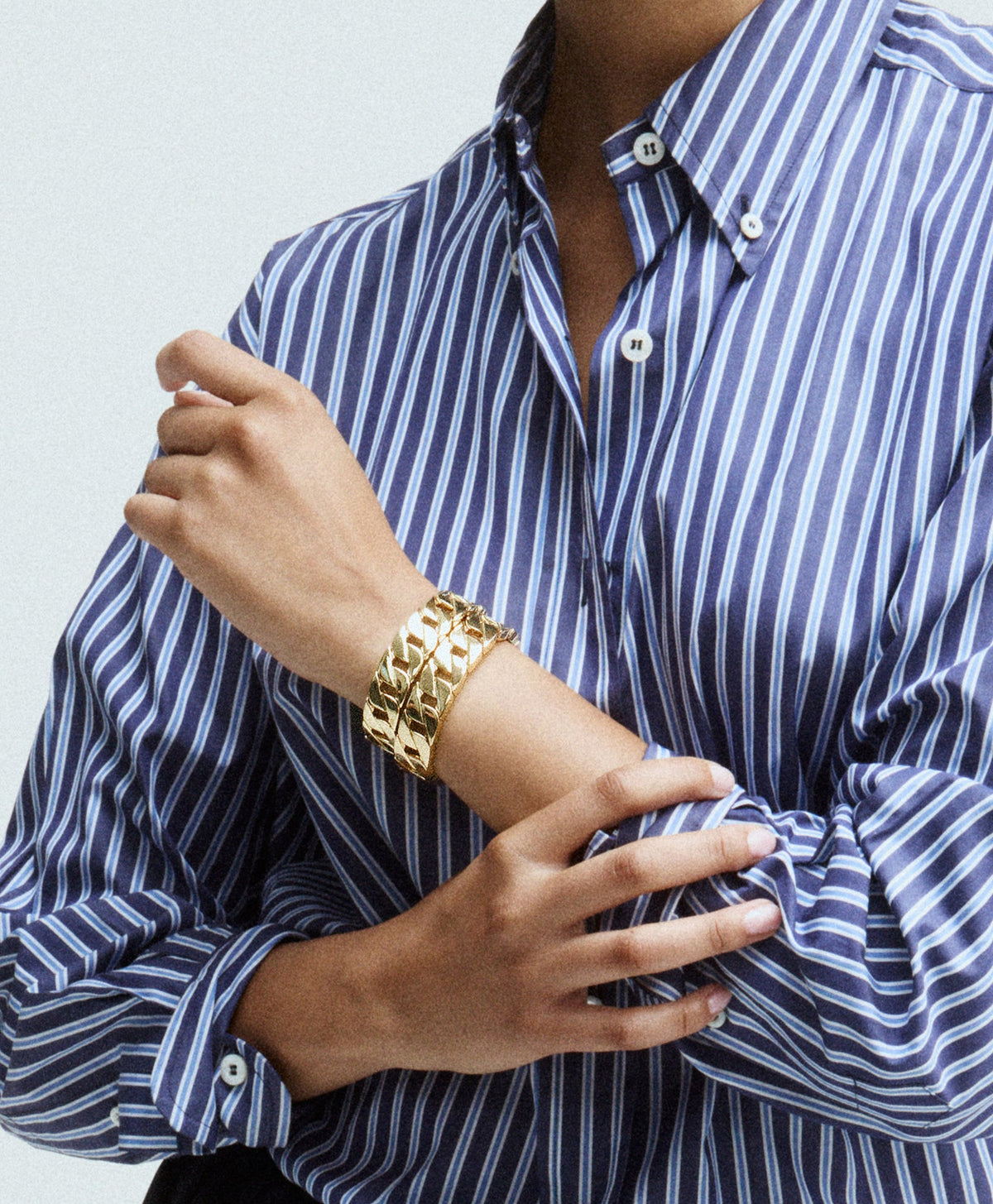 Close-up of gold tone stretch Babe Link Bracelet showcasing its linked design on a wrist with a blue striped shirt