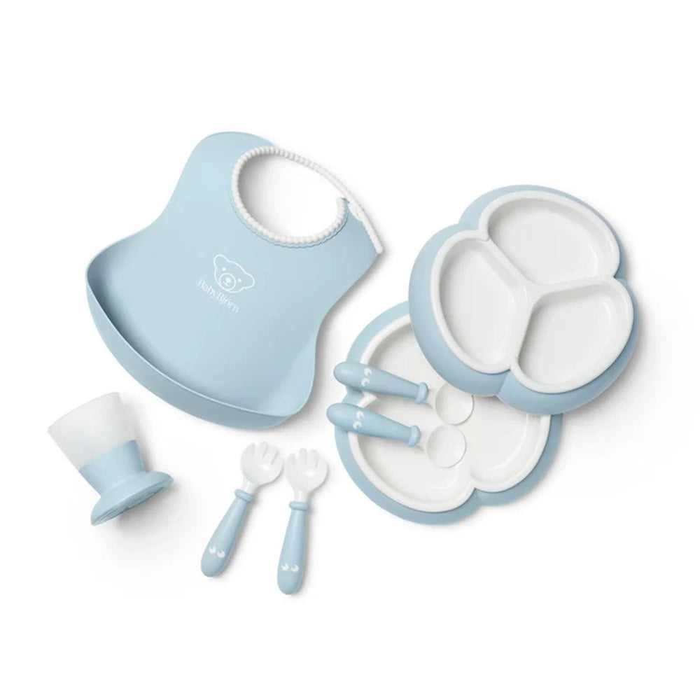 Top view of powder blue BabyBjorn dinnerware set with trefoil divided plate, bib with spill pocket, utensils, and frosted cup