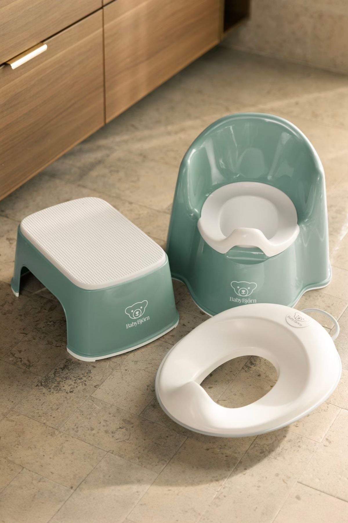 Angled view of BabyBjörn Potty Training Bundle: deep green chair, step stool with non-slip top, and white toilet seat
