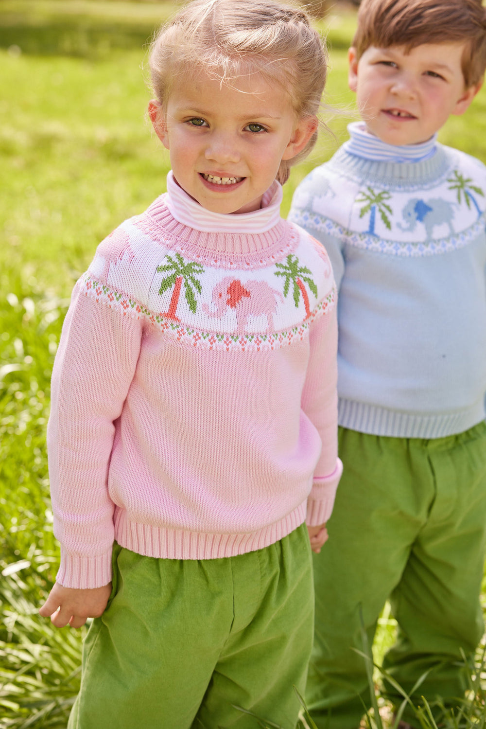 Girl wearing light pink-and-white striped turtleneck under a pink elephant sweater, standing outdoors with boy behind her
