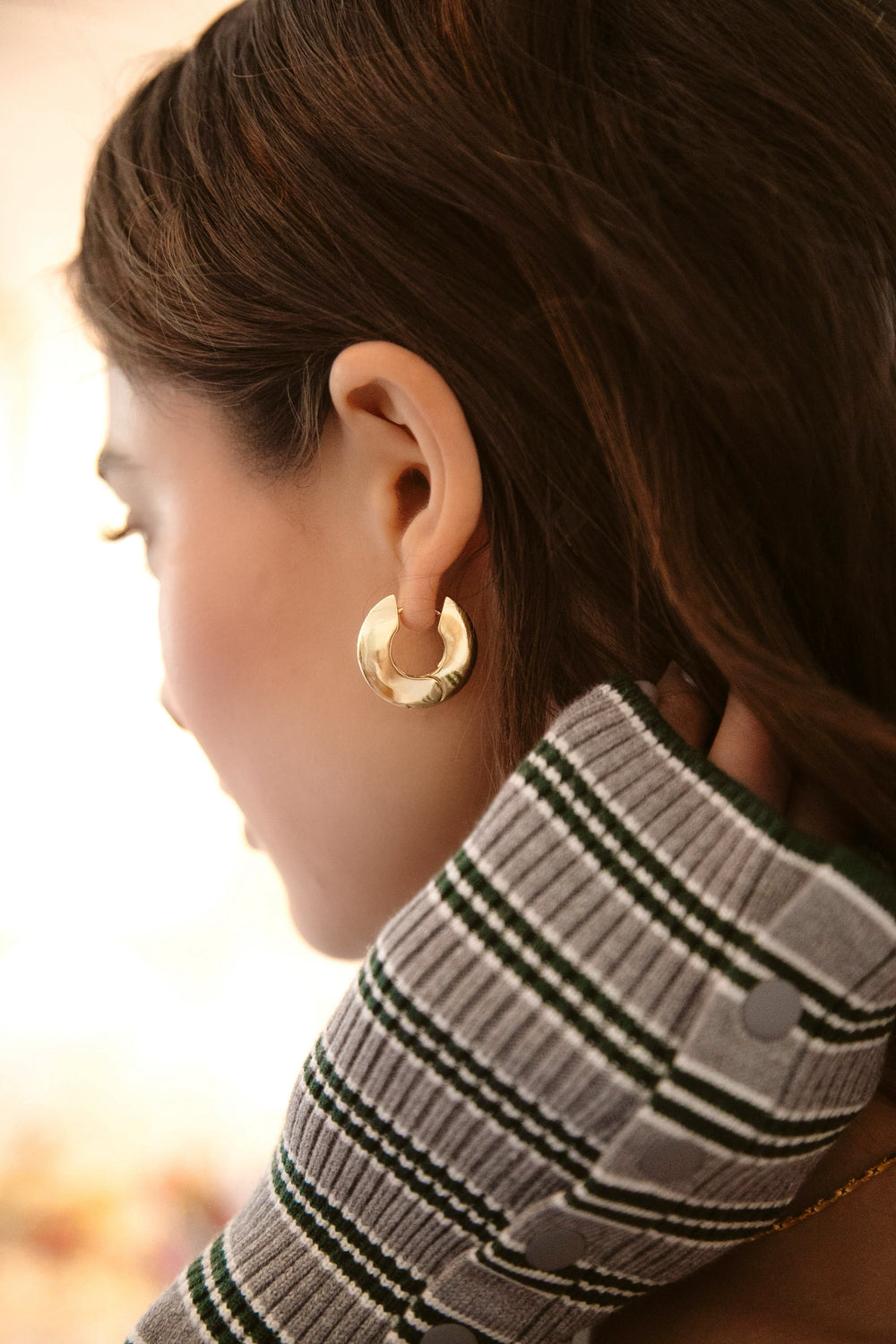 Side view of Barrel Hoops on model showing beveled edge and 24K antique gold plating with soft blurred background