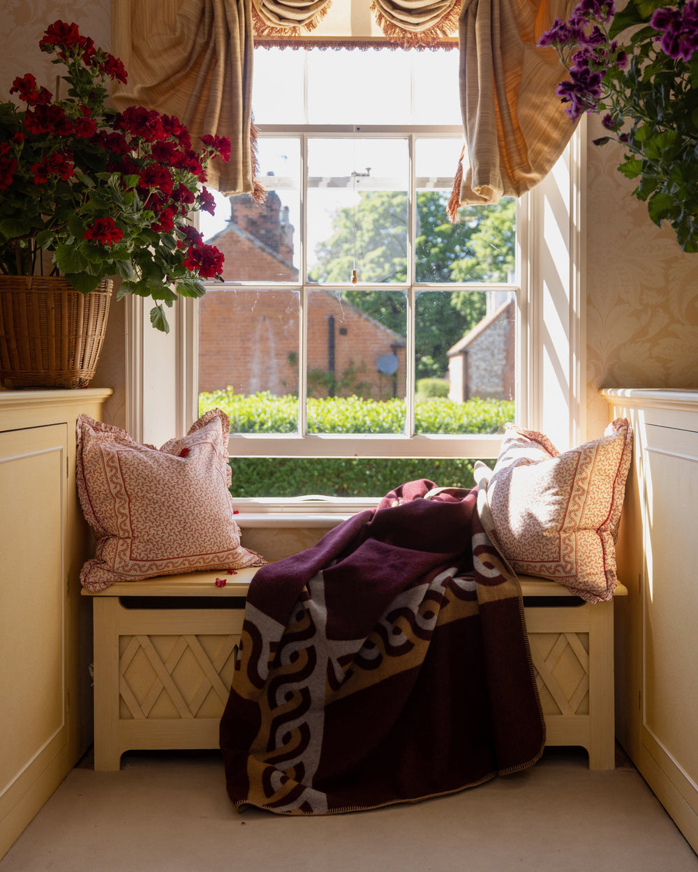Bench view of Caline cashmere blend blanket draped to show burgundy and tan Greek border and soft texture in a sunlit room