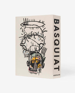 Basquiat: The World of Jean-Michel by Assouline: alternate angle showing a second Basquiat artwork on the cover — an expressive neo-expressionist portrait with a yellow-skinned skull-like face, frenetic gestural black marks, and abstracted features in Basquiat's raw signature style; BASQUIAT on the spine at right