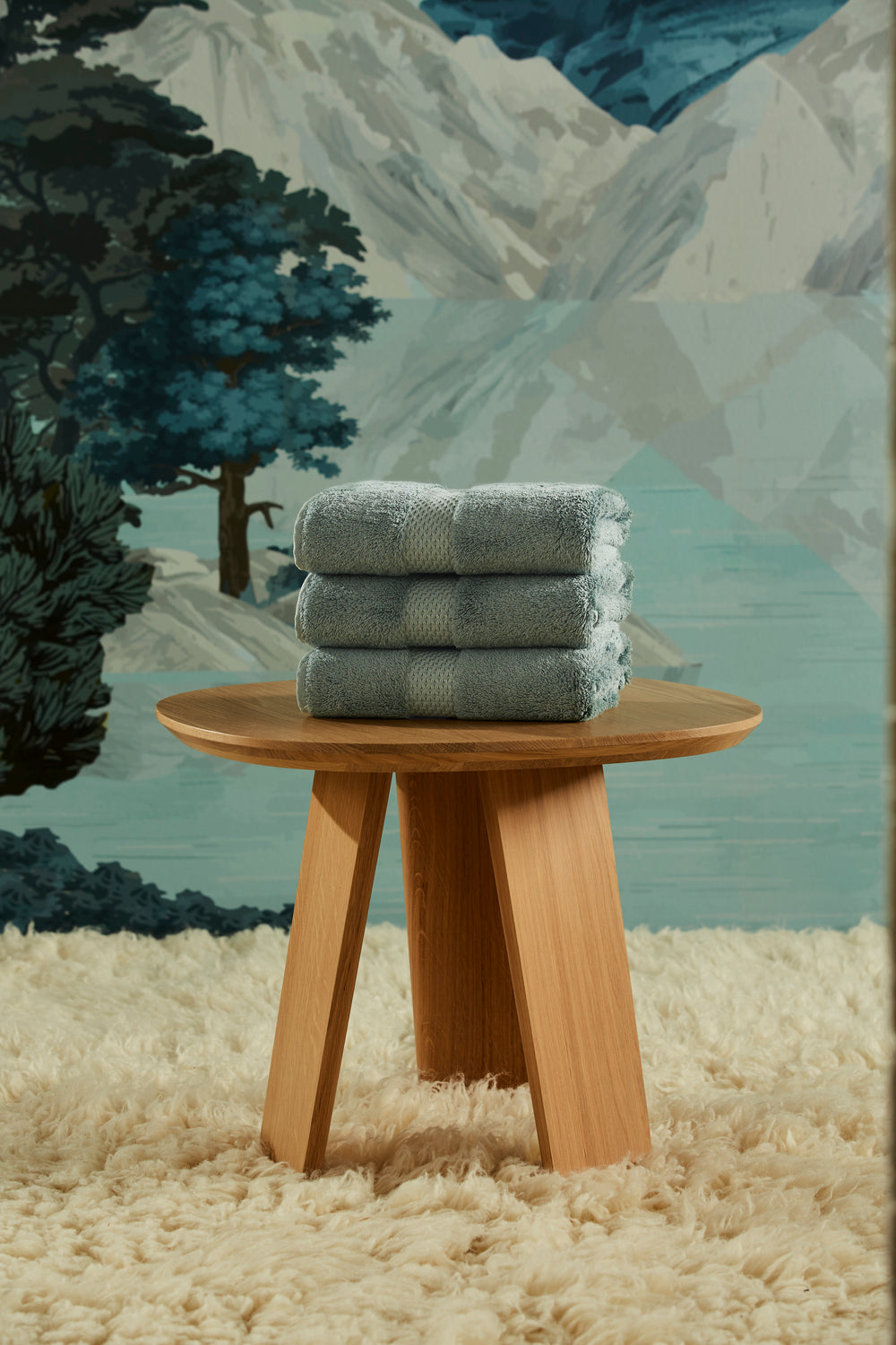 Stacked Etoile bath mats in fjord blue showing star pattern and woven border on a wooden table
