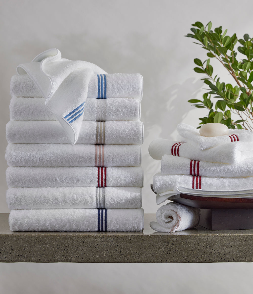 Stacked Bel Tempo bath towels showing colored stripe bands on white terry with neutral background and plant