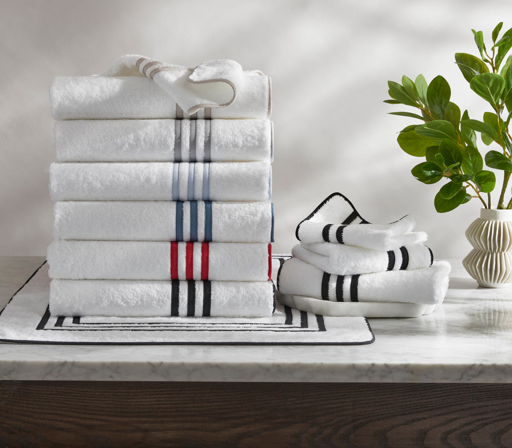 Front view of Newport Bath towels stacked, white terry with navy, red, and gray stripe trim, on marble countertop with striped mat and vase