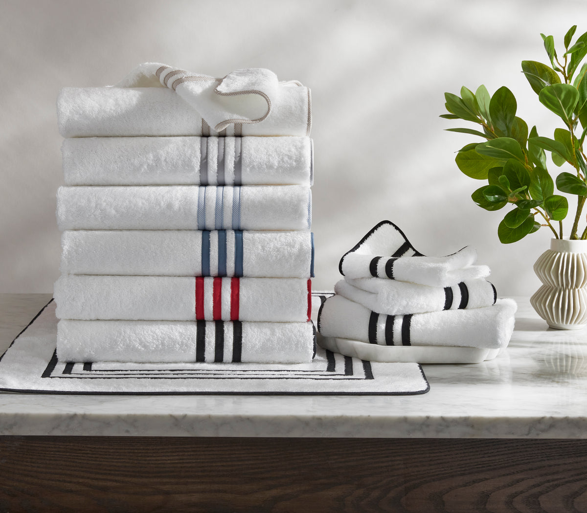 Front view of Newport Bath towels stacked, white terry with navy, red, and gray stripe trim, on marble countertop with striped mat and vase