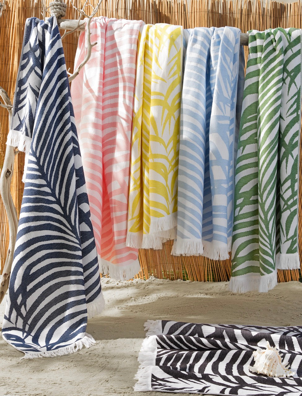 Zebra Palm beach towels in multiple colors with zebra-stripe palm pattern and white fringe against a bamboo backdrop