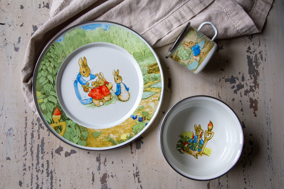 Top view of Peter Rabbit Child Set showcasing illustrated enamel mug, bowl, and plate on a distressed tabletop