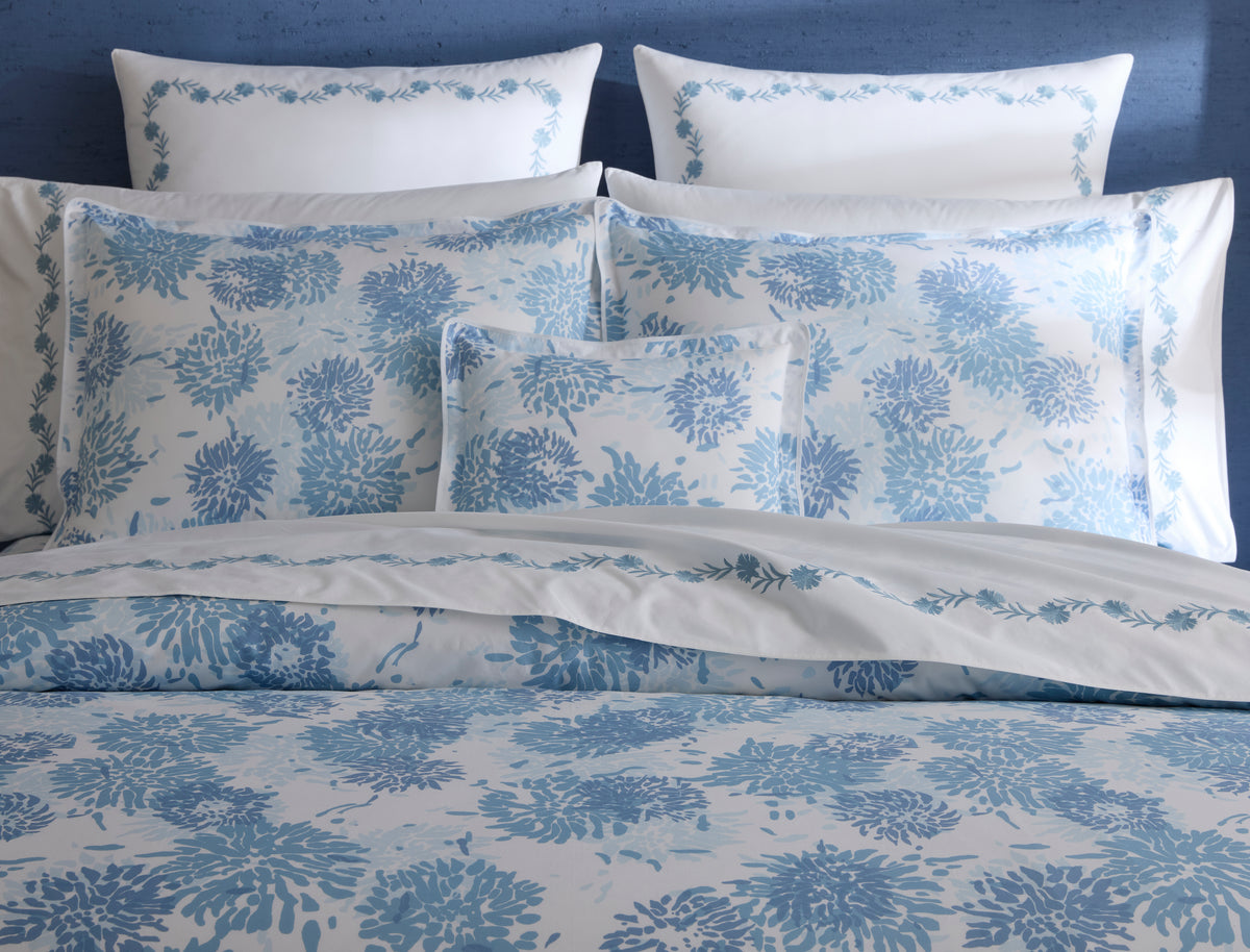 Front view of Chrysanthemum sham showcasing blue chrysanthemum floral print and piped flange on white background, styled on bed with blue headboard