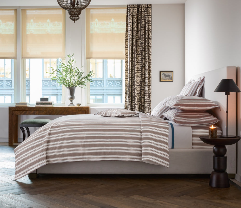 Side view of Elio quilt on a made bed showcasing mocha hand-drawn horizontal stripes on cotton percale in a bright bedroom