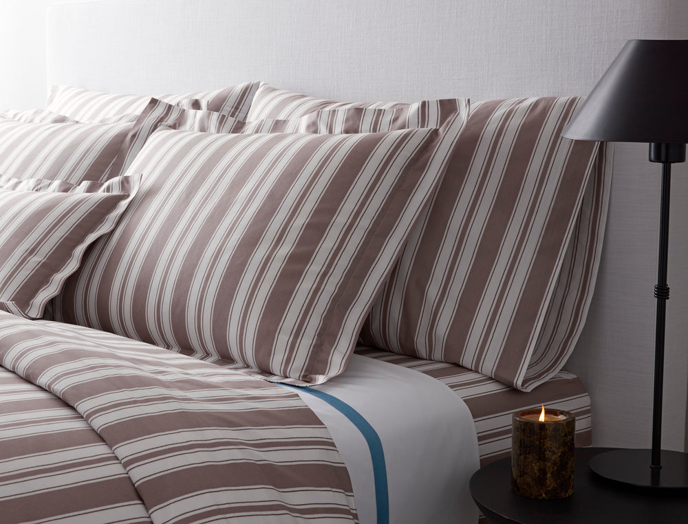 Close up of Elio pillowcases showing wide hand drawn mocha and white stripes on Egyptian cotton percale against a light upholstered headboard