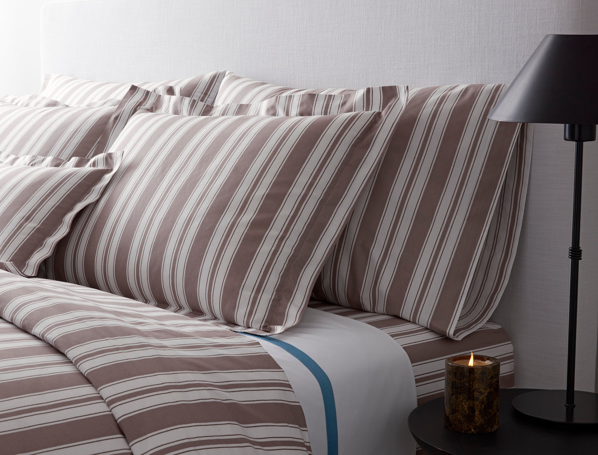 Close up of Elio pillowcases showing wide hand drawn mocha and white stripes on Egyptian cotton percale against a light upholstered headboard