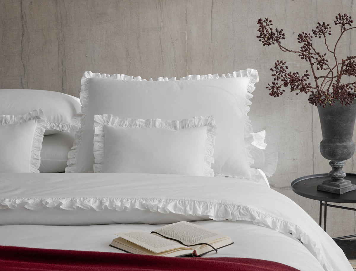 Front view of Georgia duvet cover with ruffled flange and matching shams on styled bed against concrete wall