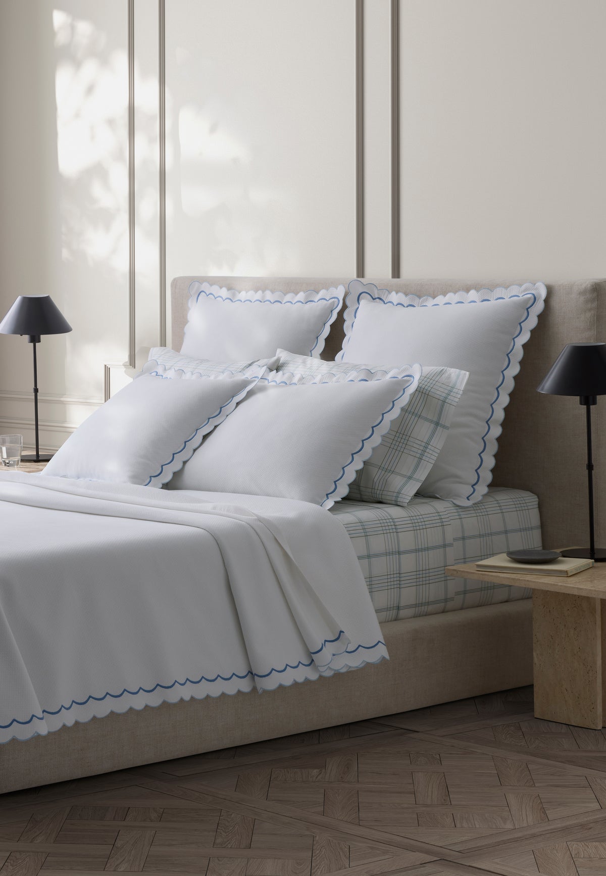 Angled view of India Pique bed skirt in azure with scalloped two tone trim on a neutral upholstered bed