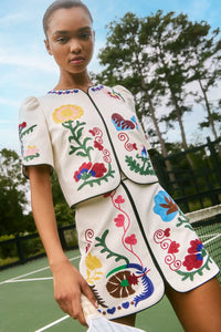 The Dottie Mini Skirt is a white A-line skirt with fitted waist and colorful hem throughout.