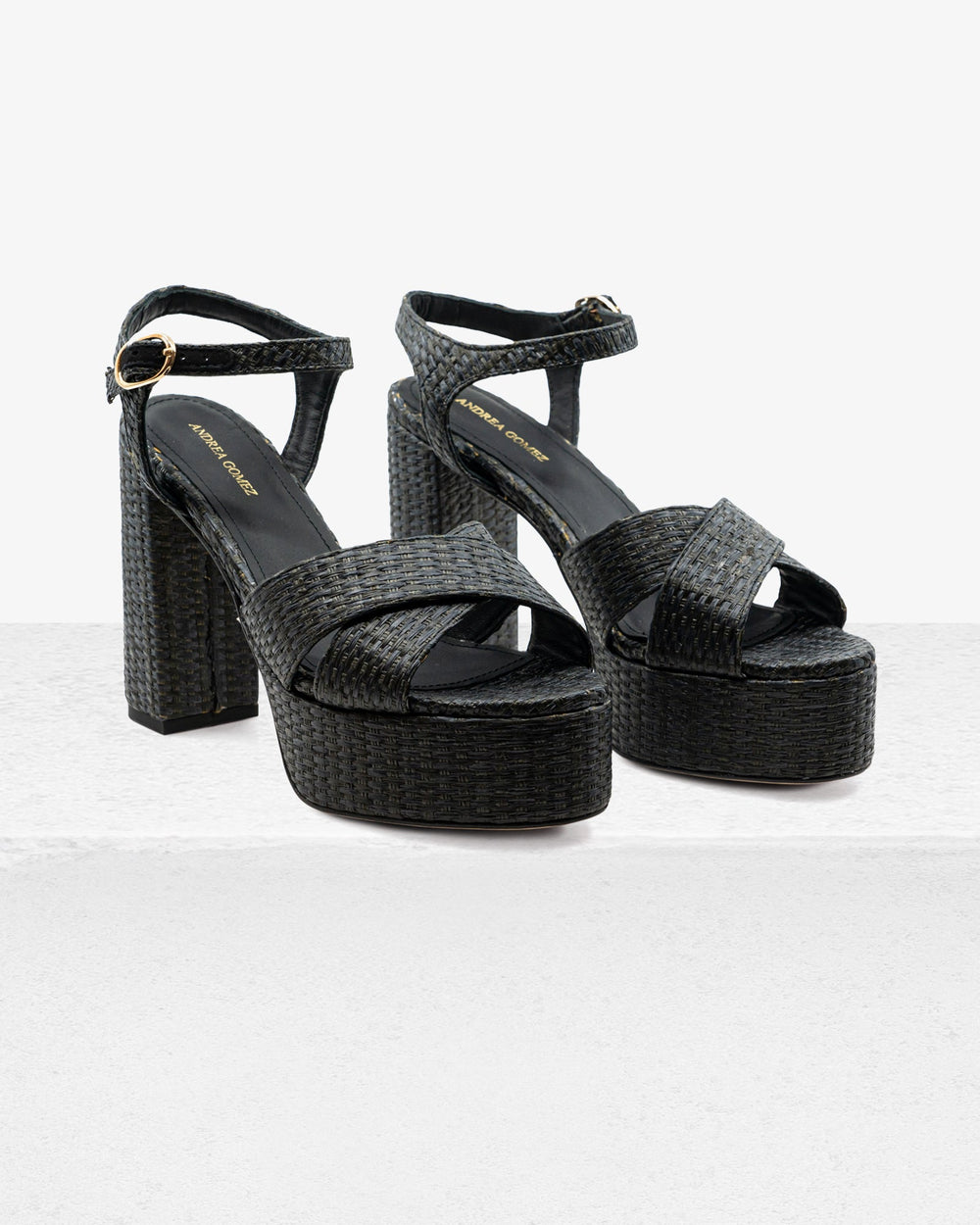 Three-quarter view of Bella Black Raffia sandals showing woven raffia, crisscross straps, buckled ankle strap and block heel