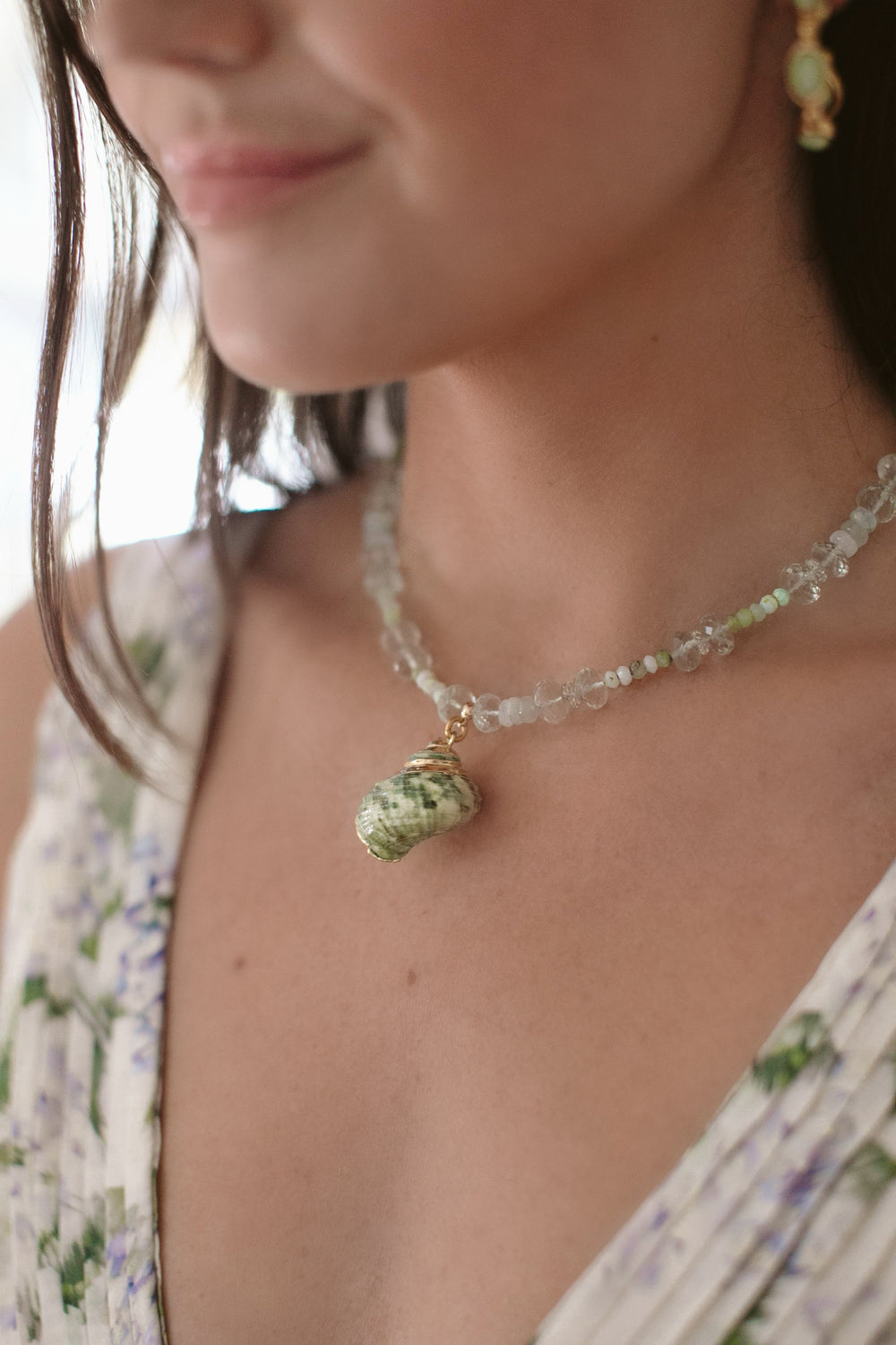 Close up of Bellamy Necklace on model showcasing green shell pendant and mixed green gemstone beads against a floral dress