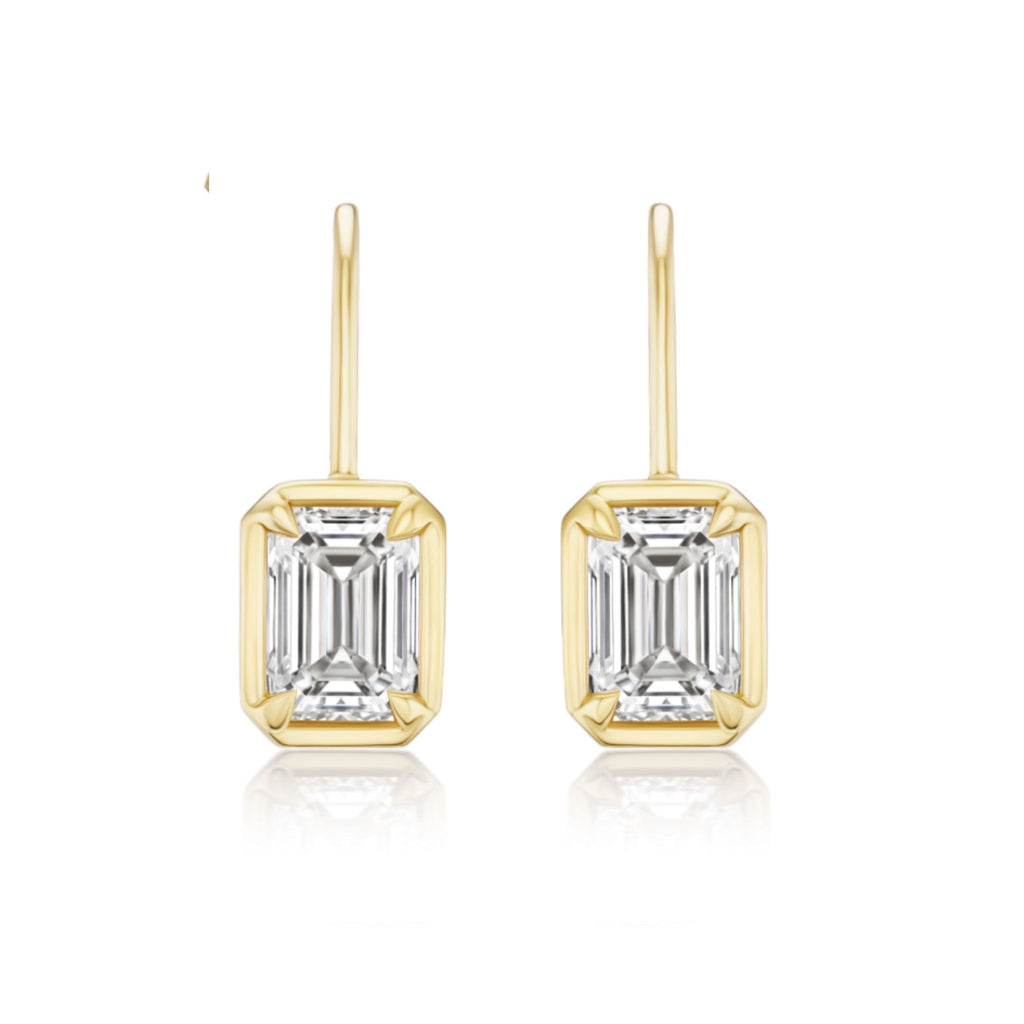 The Bezel Set Emerald Cut Diamond Ear Jacket in Yellow Gold features J-color emerald cut diamonds in rectangular gold frames, shown on a white background.